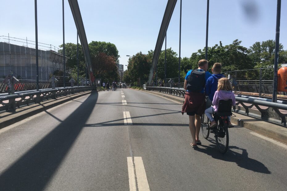 Für den Autoverkehr gesperrte Modersohnbrücke: AUf der Fahrbahn ein Erwachsener, der ein Rad schiebt, auf dem zwei Kinder sitzen.